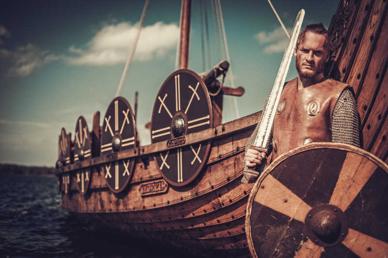 手拿着剑和盾牌的维京勇士站在海盗船前