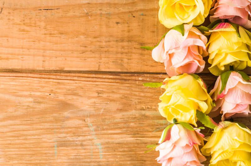 木板上放着粉色和黄色的玫瑰花