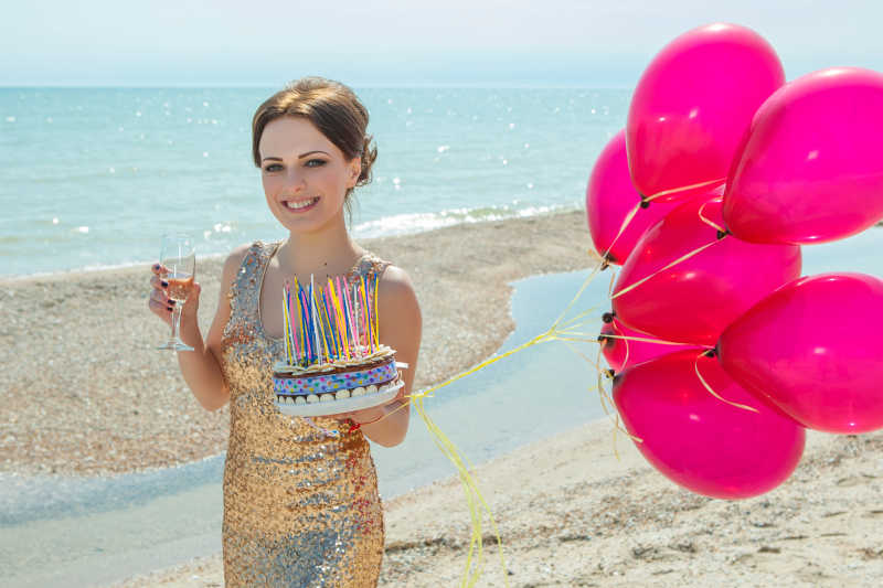 沙滩上穿着礼服端着酒杯拿着气球和蛋糕的美女