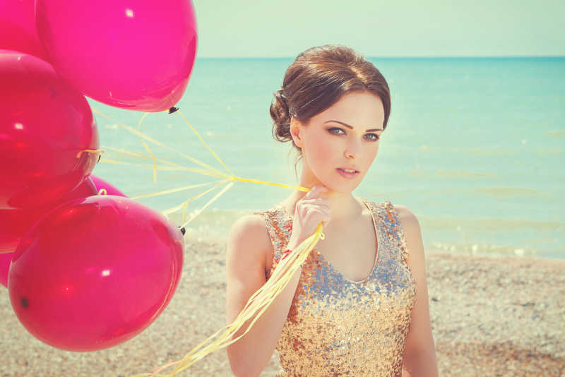 沙滩上身穿金色礼服的美女拿着气球