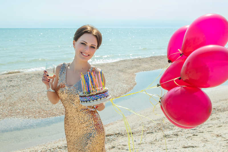 沙滩上拿着气球蛋糕和香槟酒杯的美女