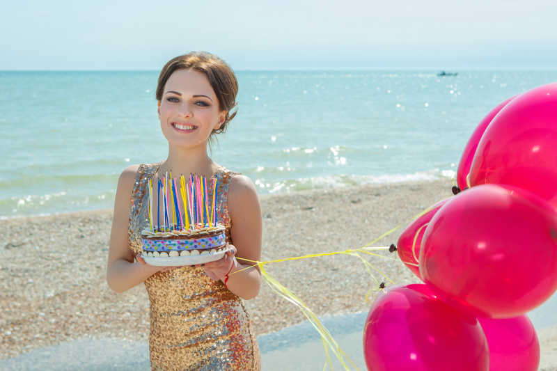 海边沙滩上拿着气球香槟和蛋糕穿着礼服的美女