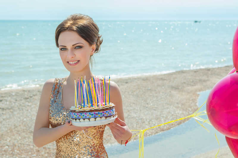 沙滩上身穿礼服的美女拿着蛋糕和气球