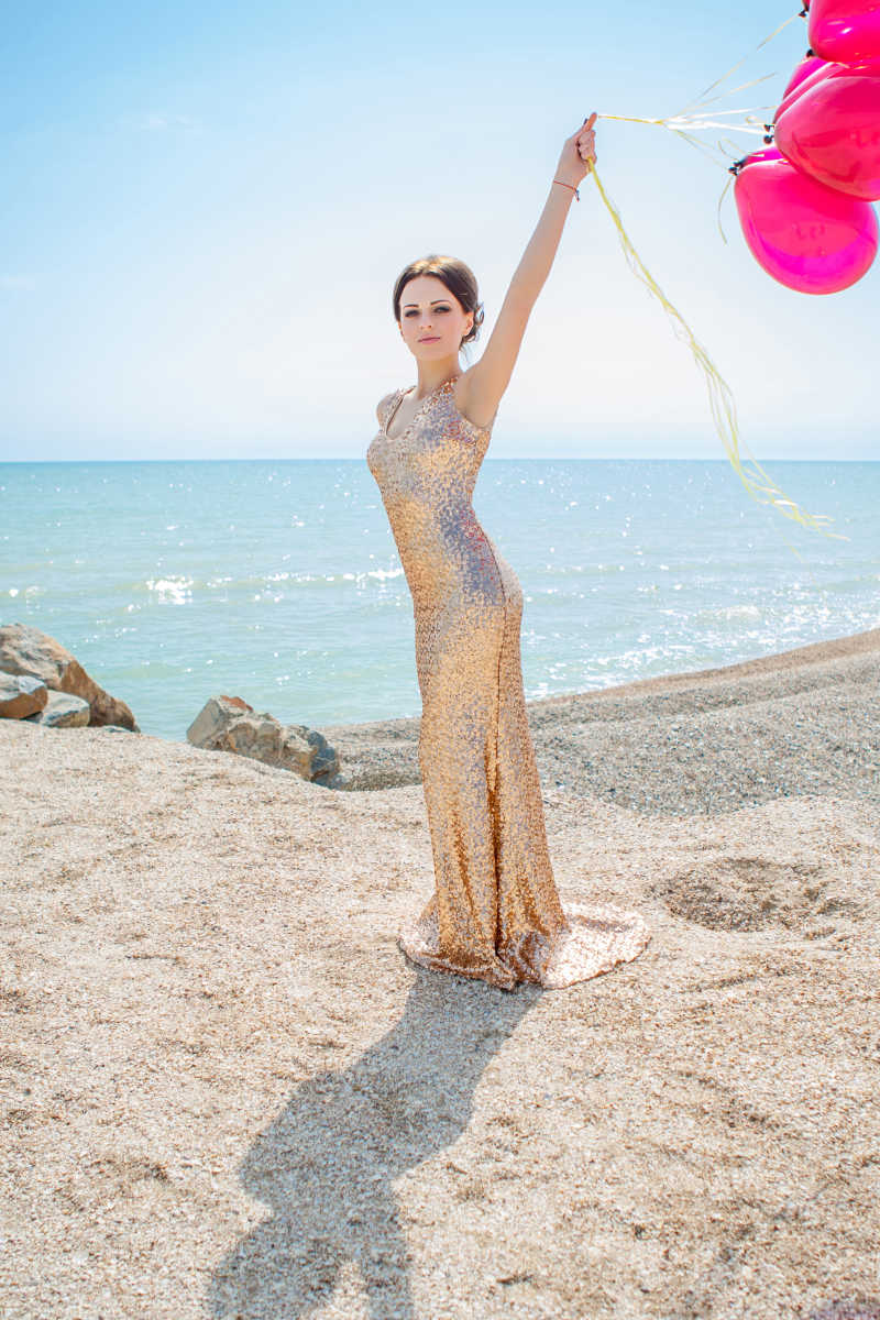 海边沙滩上身穿礼服拿着气球的美女