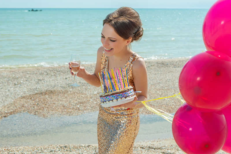 沙滩上的拿着气球酒杯和蛋糕的美女