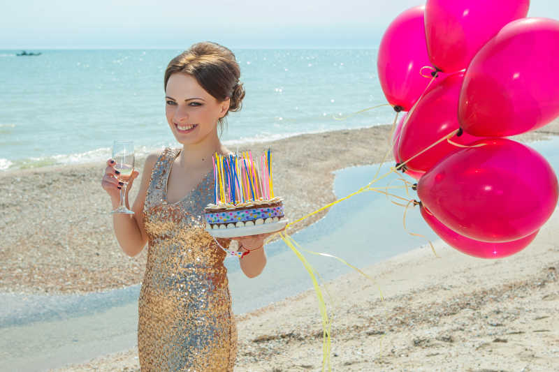 沙滩上开心的拿着蛋糕气球和酒杯的礼服美女