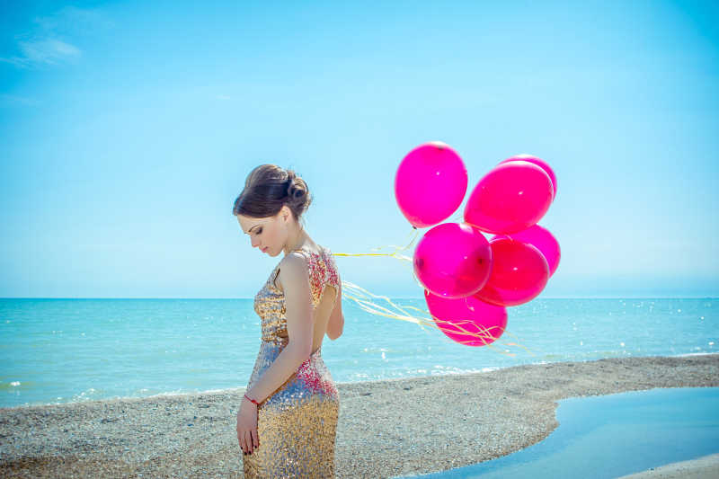 沙滩上身穿礼服的美丽女孩拿着气球