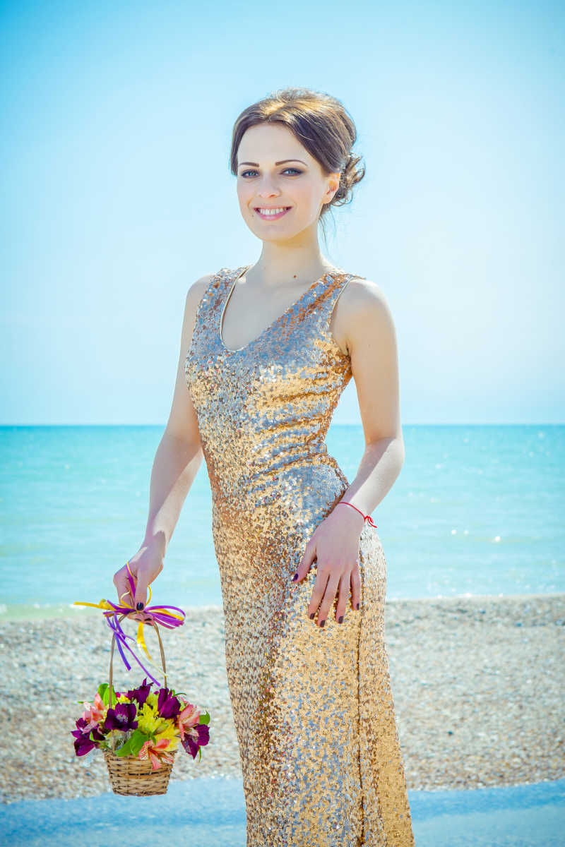 沙滩上穿着金色礼服拿着鲜花的美女