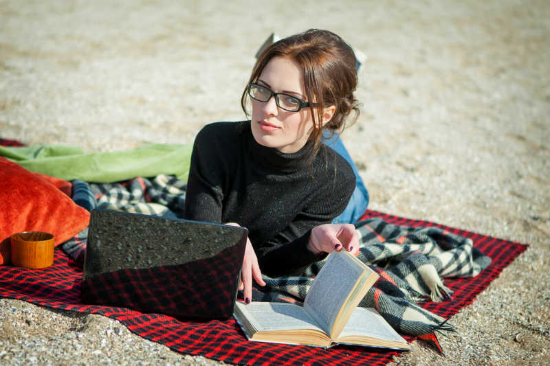 趴在沙滩上翻着书的年轻女人