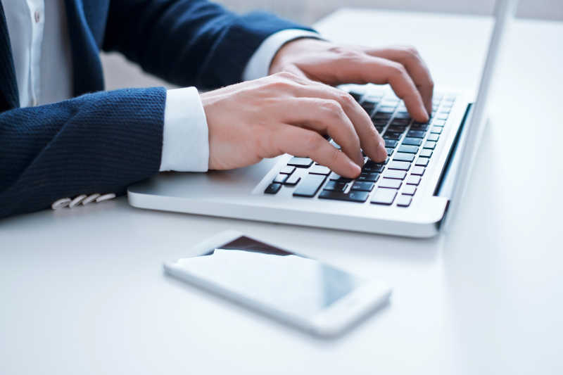 白色桌面上穿着黑衣服的人正在笔记本电脑上打字