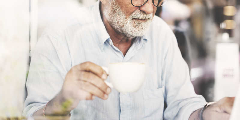 穿着白色衬衣的喝咖啡的老年商人