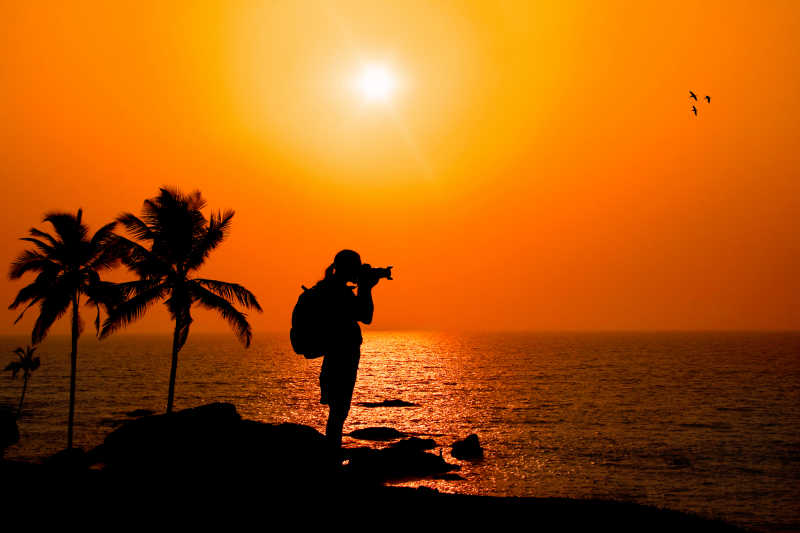 日落时站在海边拍摄的摄影师