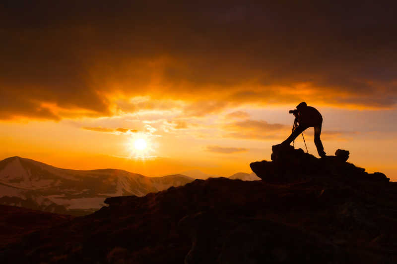 站在山顶上拍摄日落的摄影师