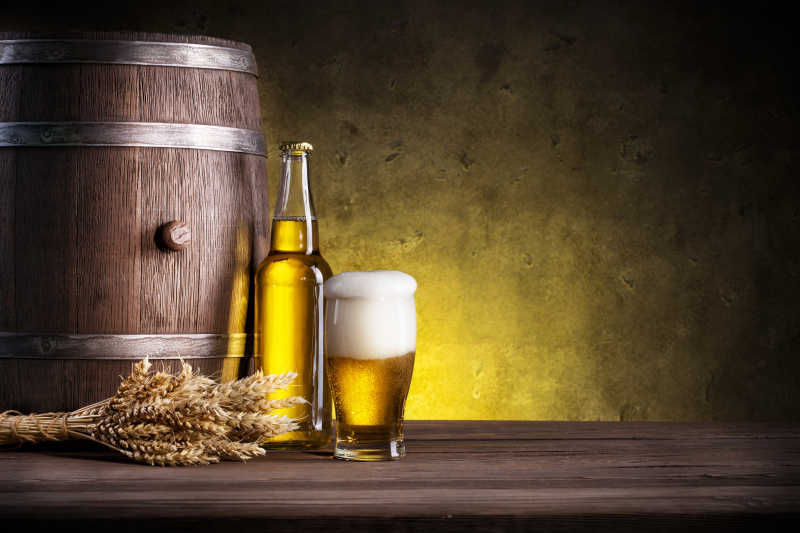 木桌上的圆筒和黄色的泡沫啤酒以及金色的麦穗