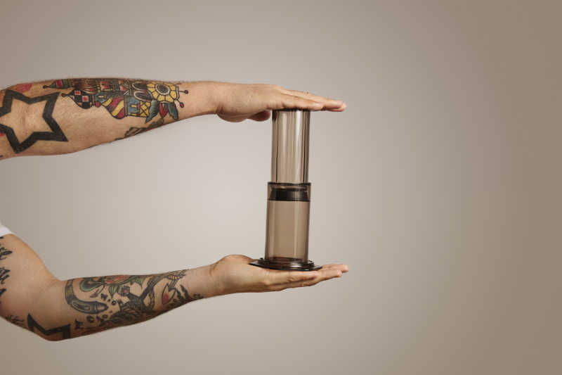浅灰色背景下手臂纹身男人双手紧贴着小型咖啡机