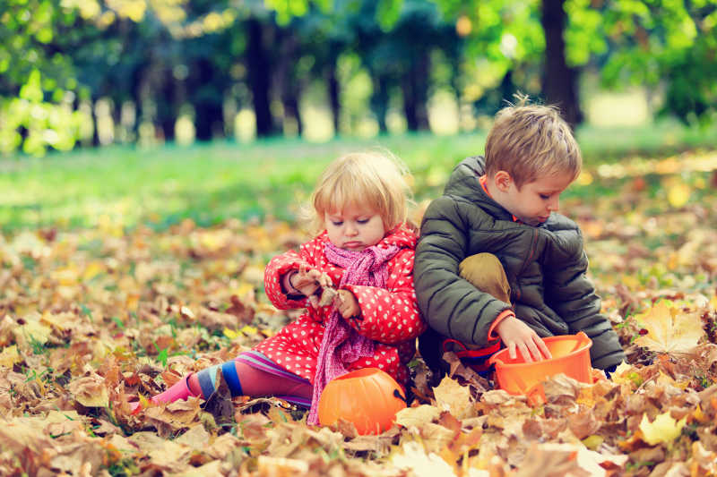 公园里一起玩落叶的庆祝万圣节的孩子