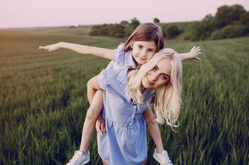 在绿色的麦田中背着小女孩的母亲