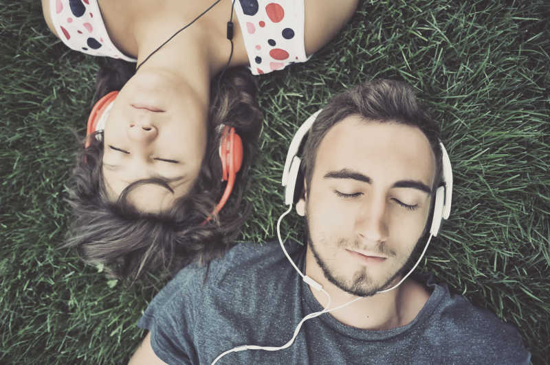 情侣躺在草地上闭着眼睛享受音乐