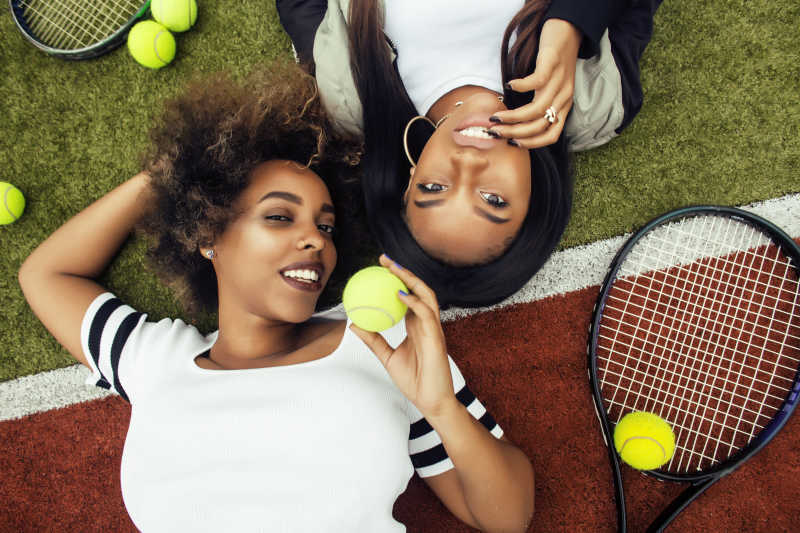 快乐的两个打网球的女孩躺在球场上