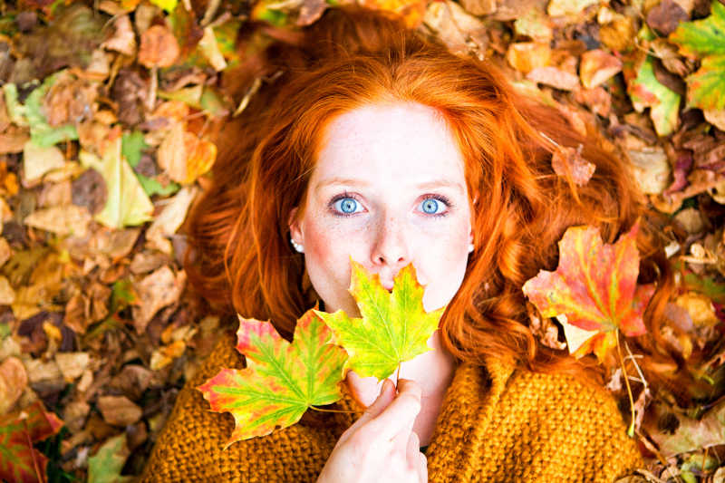 秋季美女躺在落叶上拿着两张枫叶拍照