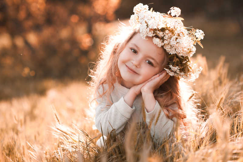蹲在草丛戴花环微笑的小女孩