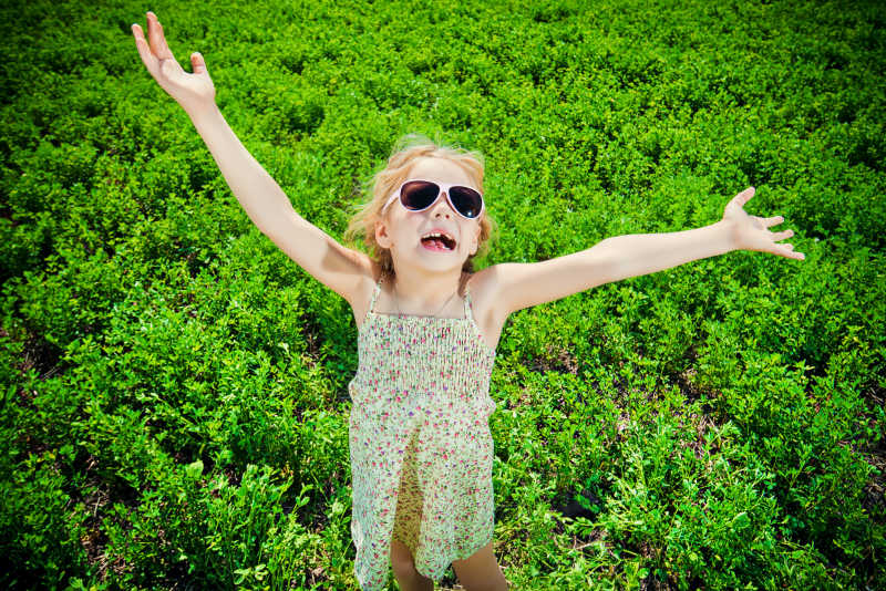 绿色草地背景下展开双臂的小女孩