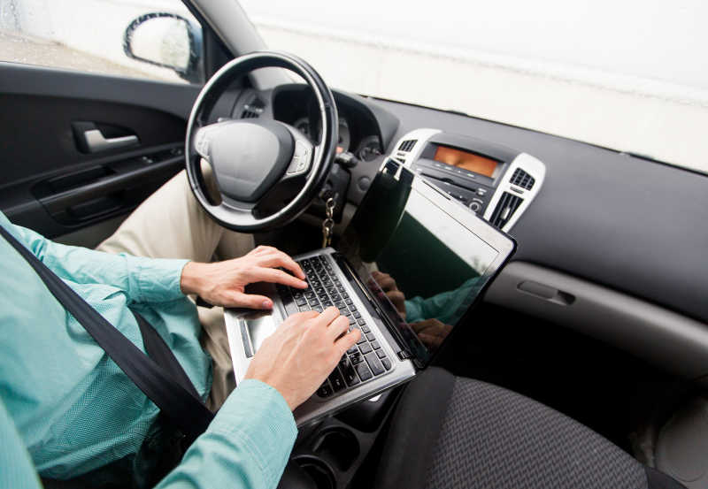 年轻男人用笔记本电脑驾驶汽车靠拢