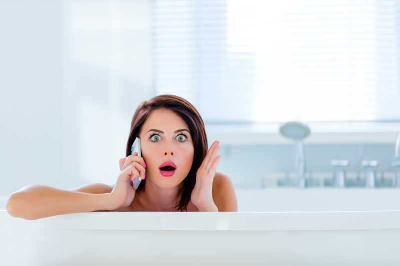 年轻女人在浴室里打电话露出惊讶的神情