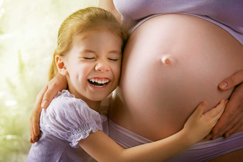 女儿将脸贴在孕妇妈妈的肚子上