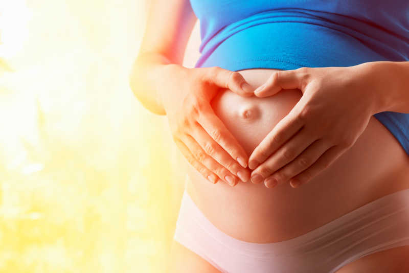 孕妇将手拼成爱心形状放在自己的肚子上
