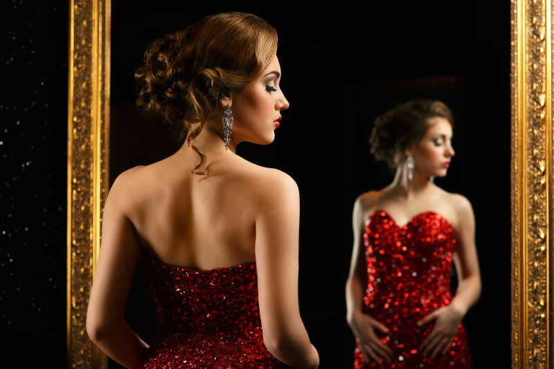 黑色环境中穿红色闪光礼服站在镜子前的性感美女