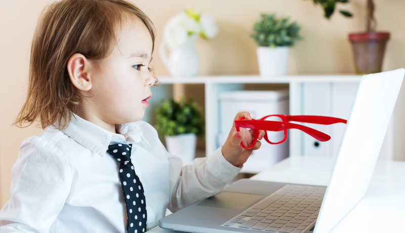大人装扮的幼儿拿着红框眼镜指着笔记本电脑屏幕