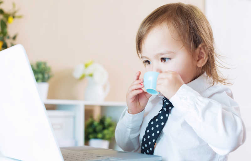 大人装扮的幼儿看着电脑喝着咖啡