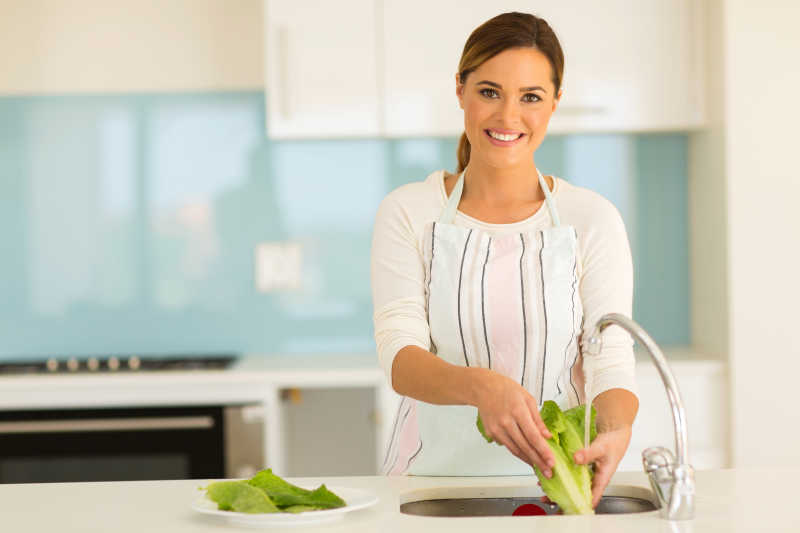 微笑的女人在洗涤槽里洗蔬菜
