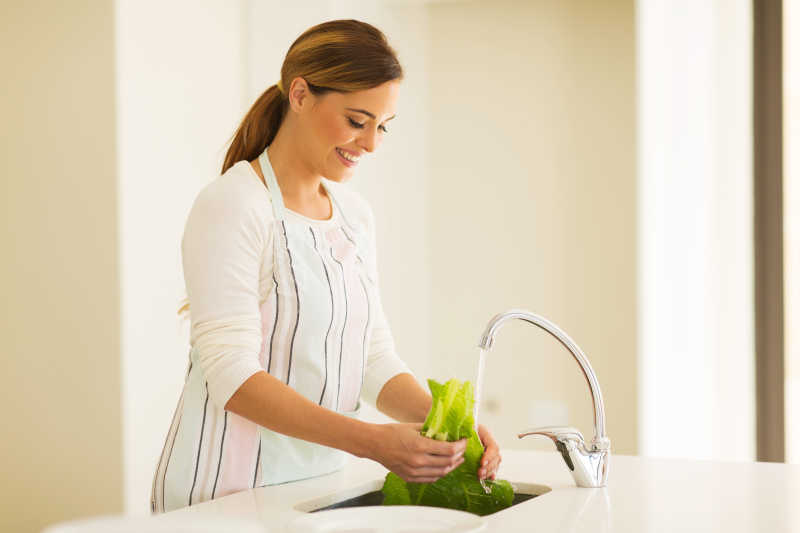 快乐的年轻女人在厨房里洗莴苣