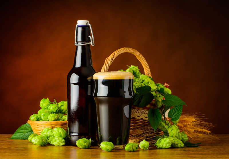 褐色背景下木桌上的一瓶黑啤酒和一些麦穗