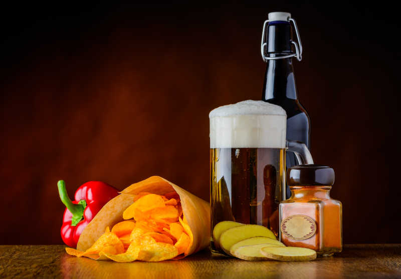 褐色背景下木桌上的一瓶啤酒一份小吃和一杯啤酒的玻璃杯