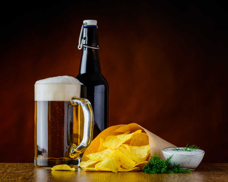 褐色背景下木桌上的一瓶啤酒和一纸袋薯条