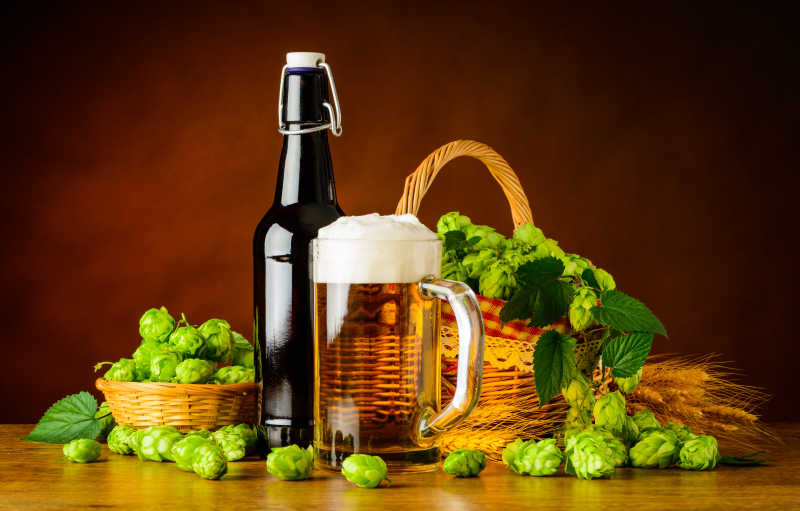 褐色背景下木桌上的一瓶啤酒和装满啤酒的玻璃杯