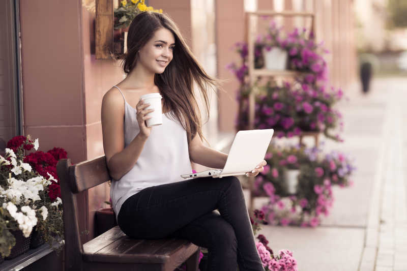 年轻女人坐在户外长椅上玩电脑