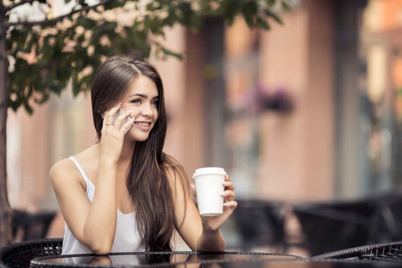 年轻漂亮的女人在户外咖啡桌上打电话