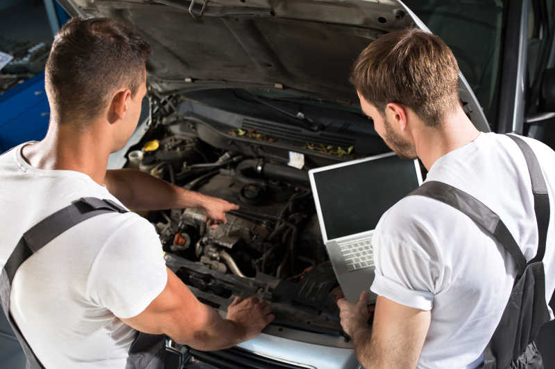 两个男性汽车修理工拿着笔记本讨论汽车修理问题