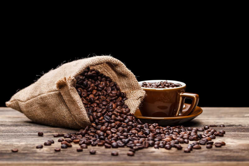 黑色背景下木桌上的一袋咖啡豆和一杯咖啡