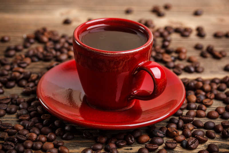 木桌上红色的咖啡杯里的咖啡和旁边的咖啡豆