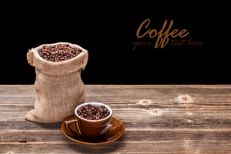 黑色背景下木桌上袋装的咖啡豆和咖啡杯里的咖啡豆