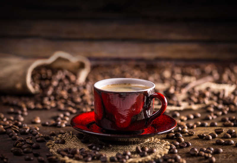 木桌上红色咖啡杯里的新鲜的咖啡和散落的咖啡豆