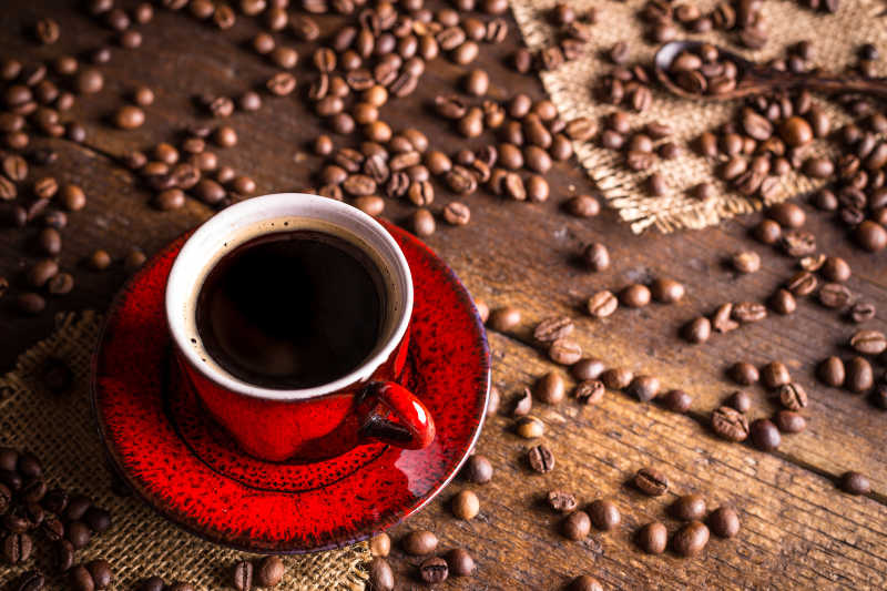 木桌上红色的咖啡杯和散落的咖啡豆