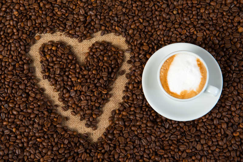 美味的咖啡和旁边摆成心形形状的咖啡豆