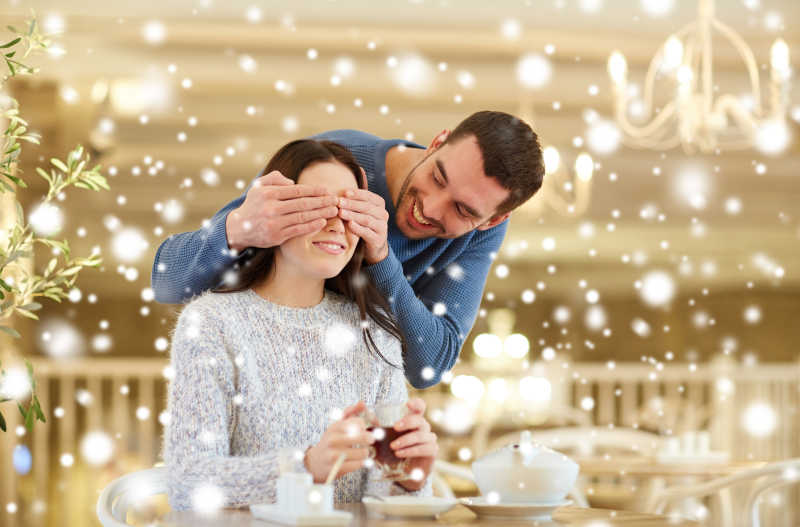 在咖啡馆或餐厅喝茶的幸福的夫妇丈夫蒙住妻子的双眼