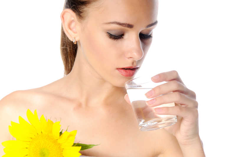 拿着向日葵和玻璃水杯喝水的年轻美女